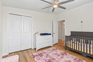 Bedroom with a closet, light wood finished floors, a nursery area, and ceiling fan