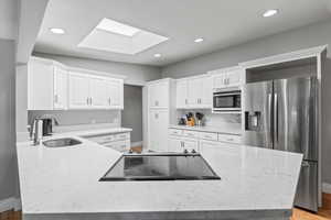 Kitchen featuring stainless steel appliances, a skylight, white cabinets, recessed lighting, and light stone countertops