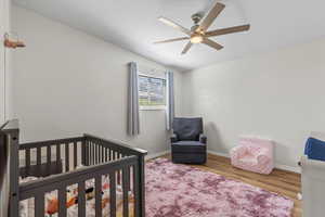 Bedroom featuring a crib, wood finished floors, lofted ceiling, and a ceiling fan