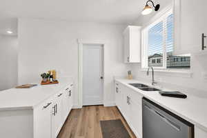 Kitchen featuring dishwasher, a peninsula, light wood finished floors, light countertops, and white cabinetry