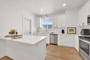 Kitchen with appliances with stainless steel finishes, white cabinets, light countertops, light wood-type flooring, and recessed lighting