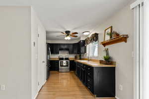 Kitchen with appliances with stainless steel finishes, dark cabinetry, ceiling fan, light wood finished floors, and light countertops