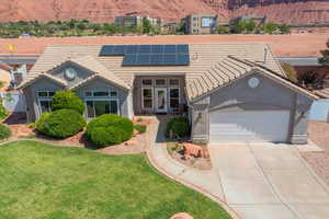View of front of house featuring a tiled roof, solar panels, driveway, an attached garage, and a front yard