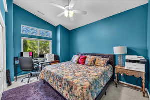 Carpeted bedroom with an office area, ceiling fan, and high vaulted ceiling