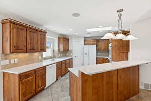 Kitchen with white appliances, a skylight, a peninsula, brown cabinetry, and backsplash