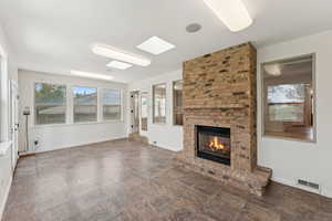 Unfurnished living room with a brick fireplace, stone finish floors, and a skylight