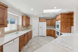 Kitchen featuring white appliances, a skylight, open shelves, backsplash, and brown cabinets