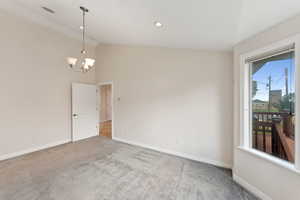 Empty room with carpet floors, a chandelier, and high vaulted ceiling