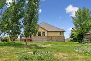Back of property with a deck, a yard, stucco siding, and brick siding