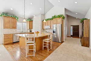 Kitchen featuring appliances with stainless steel finishes, a center island, light countertops, light wood-style floors, and high vaulted ceiling