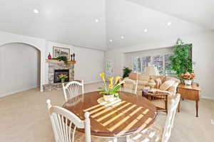 Dining room featuring light colored carpet, a stone fireplace, recessed lighting, and high vaulted ceiling