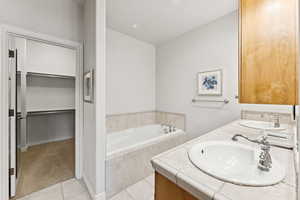 Full bathroom with tile patterned flooring, a jetted tub, double vanity, and a spacious closet