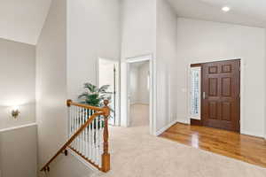 Carpeted foyer featuring high vaulted ceiling and baseboards