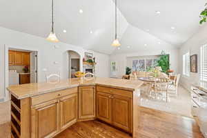 Kitchen with vaulted ceiling, washer / clothes dryer, a fireplace, light wood-style flooring, and arched walkways
