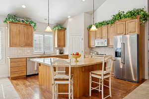 Kitchen featuring appliances with stainless steel finishes, light wood-type flooring, a center island, tasteful backsplash, and decorative light fixtures