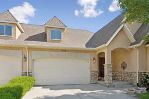 Townhome / multi-family property with stone siding, driveway, stucco siding, and a shingled roof