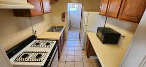 Kitchen with premium range hood, white appliances, light countertops, light tile patterned floors, and brown cabinets
