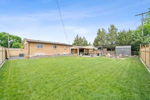 Rear view of property with a fenced backyard, a storage shed, brick siding, and a patio area