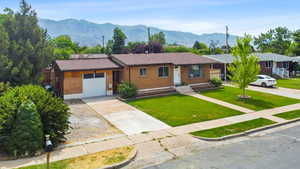 Ranch-style house featuring brick siding, an attached garage, driveway, a front lawn, and a mountain view