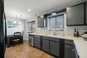 Kitchen featuring stainless steel dishwasher, light countertops, a chandelier, hanging light fixtures, and freestanding refrigerator