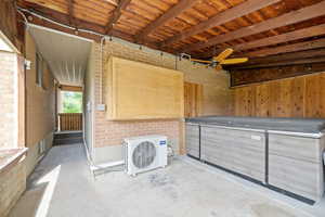 Misc room featuring concrete flooring, brick wall, ceiling fan, and beamed ceiling