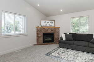 Carpeted living room featuring healthy amount of natural light, lofted ceiling, a fireplace, and recessed lighting