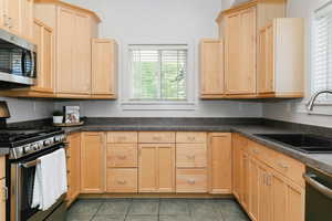 Kitchen featuring appliances with stainless steel finishes, light brown cabinetry, dark countertops, and tile patterned flooring