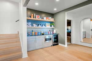 Indoor dry bar featuring wine cooler, light wood-style floors, stairs, arched walkways, and recessed lighting