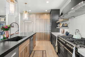 Kitchen with wall chimney exhaust hood, light wood finished floors, recessed lighting, open shelves, and hanging light fixtures