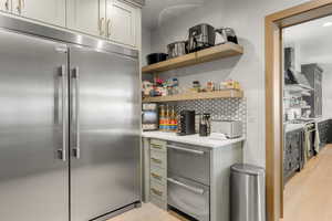 Butlers pantry with stainless steel built in fridge, wall chimney exhaust hood, open shelves, stove, and light wood-style floors