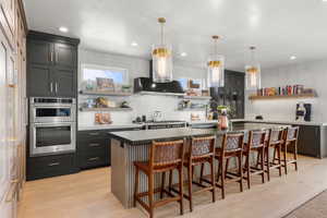 Kitchen with open shelves, stainless steel appliances, a breakfast bar area, tasteful backsplash, and light wood-style flooring