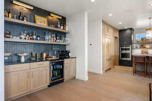 Indoor bar featuring wine cooler, stainless steel, light wood finished floors, recessed lighting, and backsplash