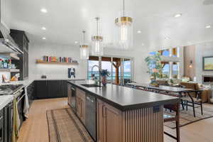 Kitchen featuring appliances with stainless steel finishes, open shelves, recessed lighting, a center island with sink, and light wood-style floors