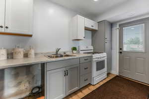 Kitchen with white gas range, updated cabinetry, light wood finished floors, and light countertops