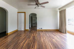 Empty room featuring ceiling fan, arched walkways, dark wood-style flooring, and a textured ceiling
