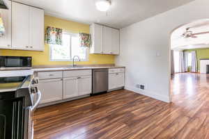 Kitchen featuring stainless steel appliances, ceiling fan, dark wood-style floors, and arched walkways