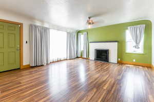Unfurnished living room featuring a ceiling fan, wood finished floors, and a fireplace