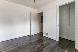 Unfurnished bedroom with electric panel, dark wood finished floors, and a closet