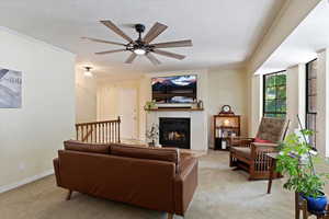 Living area featuring light colored carpet, ceiling fan, a fireplace, ornamental molding, and a textured ceiling
