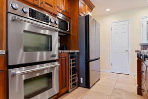 Kitchen featuring appliances with stainless steel finishes, light tile patterned floors, beverage cooler, brown cabinets, and crown molding