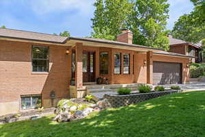 Single story home with brick siding, a garage, a front yard, a chimney, and driveway