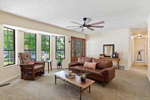 Living area featuring a ceiling fan, light colored carpet, ornamental molding, and a textured ceiling