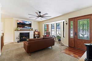 Living room featuring ceiling fan, a fireplace, ornamental molding, a textured ceiling, and light colored carpet