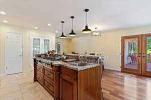 Kitchen with french doors, stainless steel gas stovetop, brown cabinets, pendant lighting, and ornamental molding
