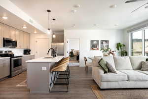 Kitchen featuring stainless steel appliances, open floor plan, a kitchen bar, backsplash, and wood finished floors