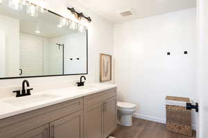 Full bathroom featuring double vanity, wood finished floors, and a tile shower
