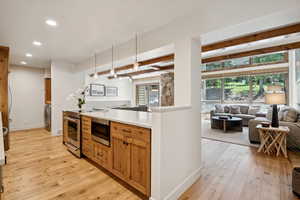 Kitchen featuring open floor plan, recessed lighting, stainless steel appliances, light wood-type flooring, and beam ceiling