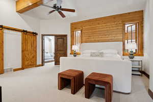 Bedroom featuring a barn door, light carpet, wooden walls, a ceiling fan, and beam ceiling