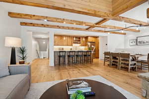 Living room featuring wet bar, beam ceiling, and light wood-style floors
