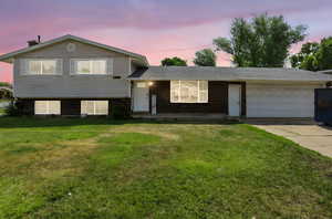 Tri-level home featuring a garage, brick siding, a lawn, and concrete driveway